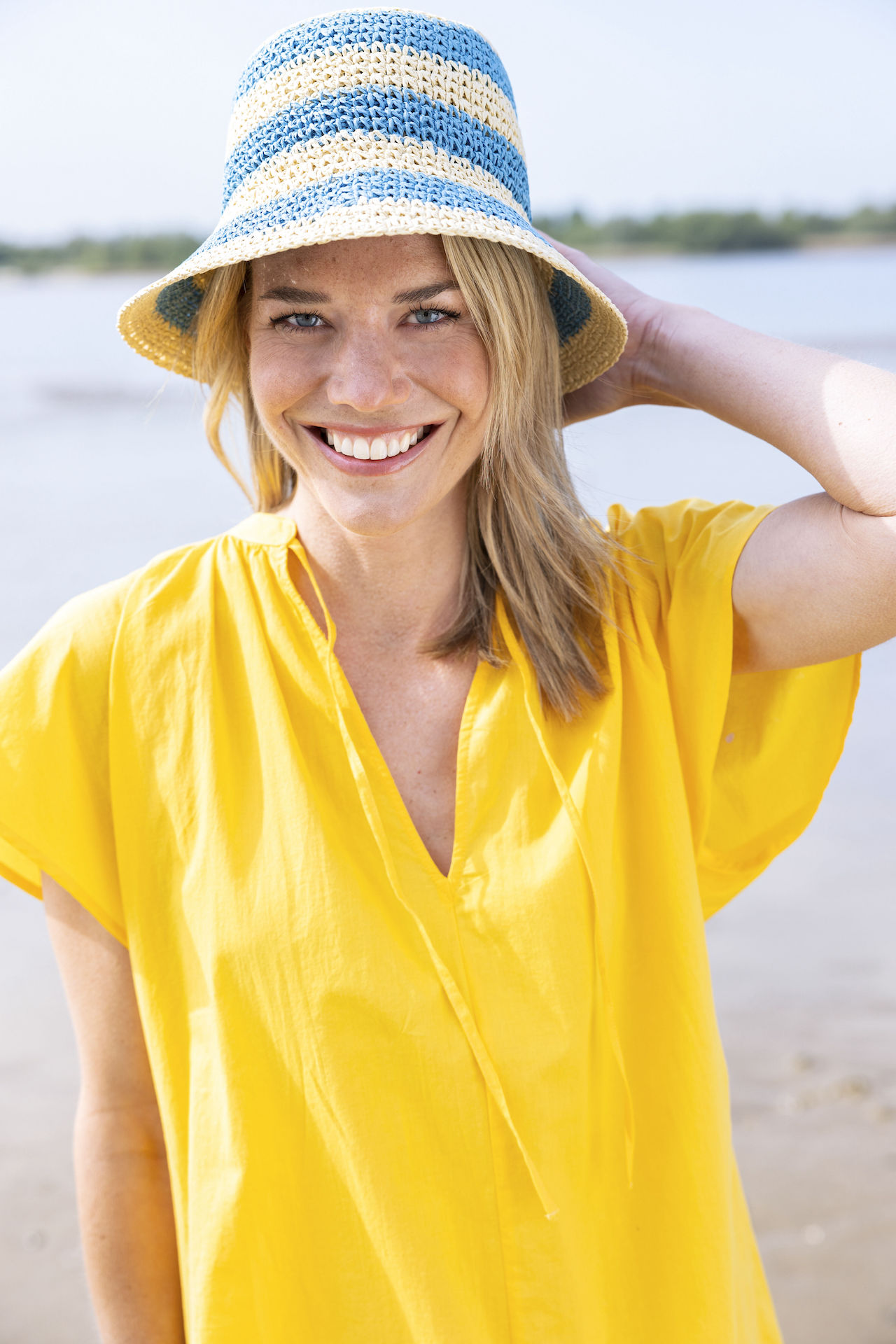 Blonde Frau in einem gelben Sommerkleid und mit Sommerhut an einem Strand