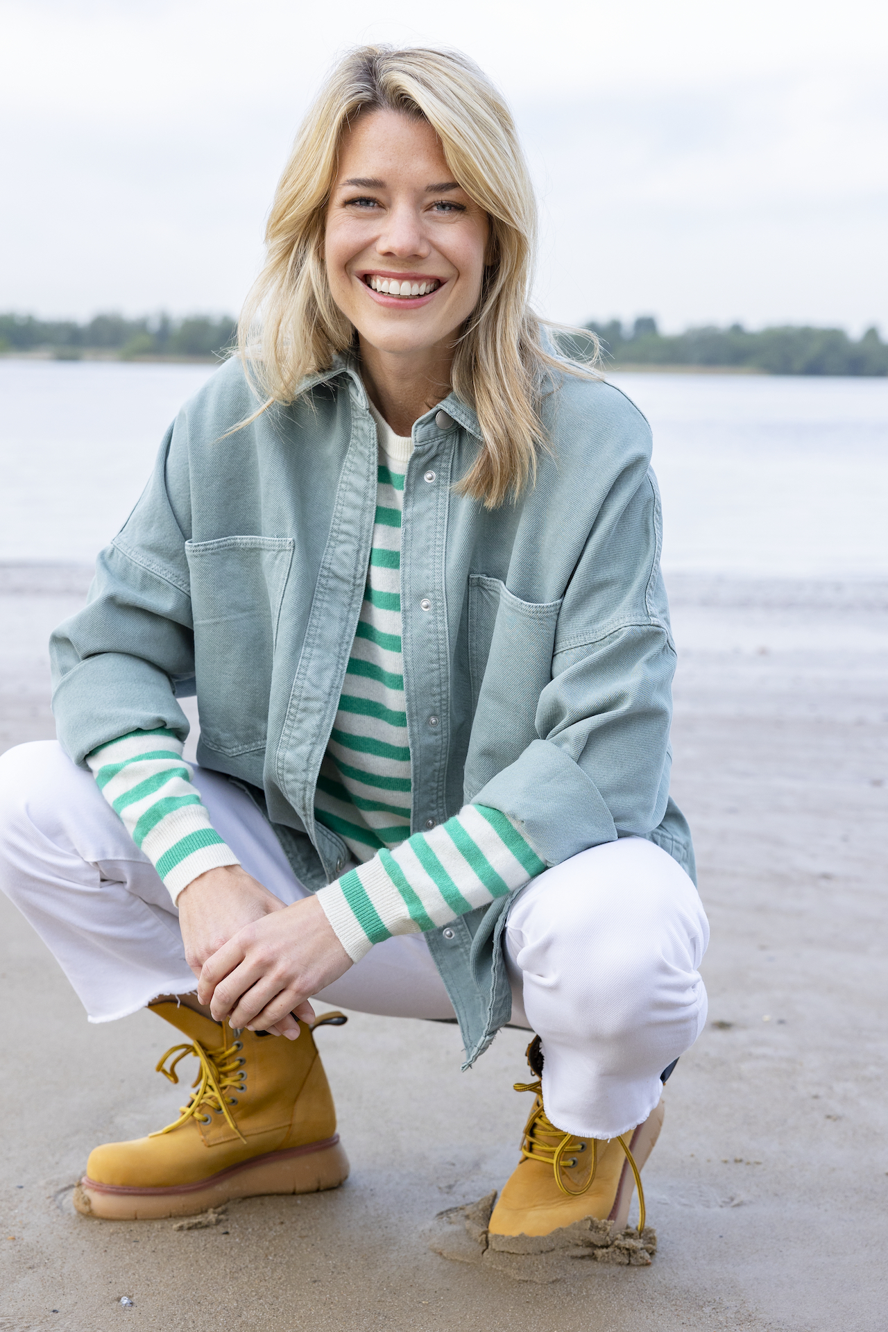 Blonde Frau in einer t¸rkisen Jacke und gestreiftem Shirt an einem Strand